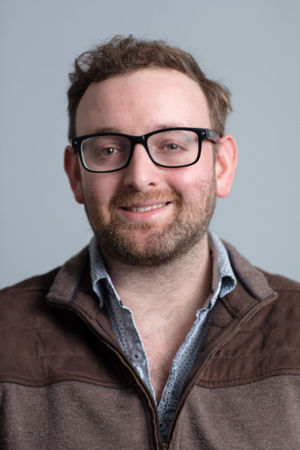 Headshot of Matt Caplan wearing a brown quarter-zip and black glasses.